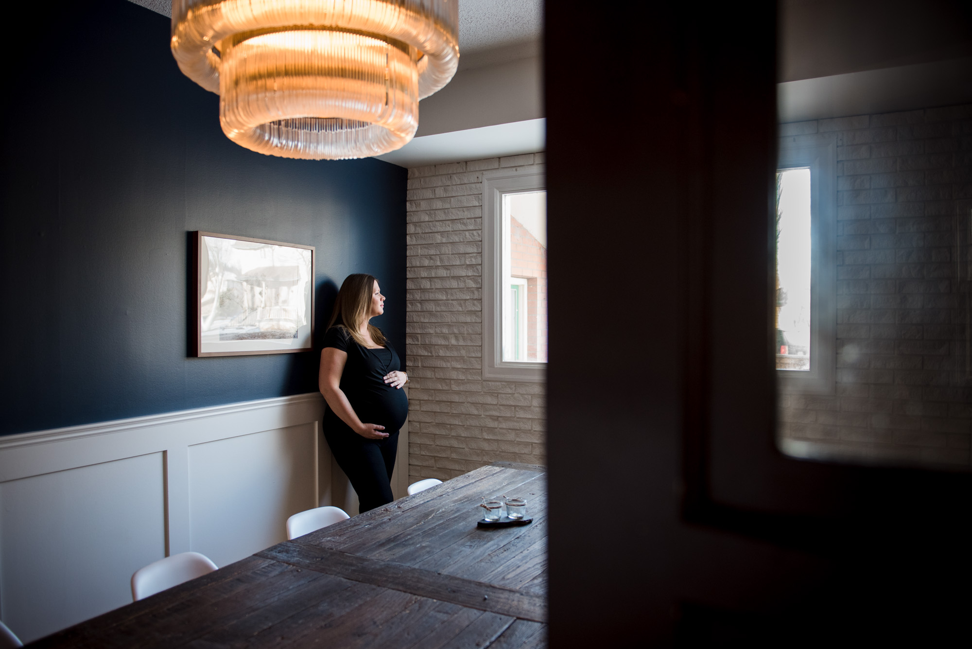 A pregnant woman gazes out a window. Photo by Fiddle Leaf Photography, clothing by Yo Mama Maternity. 