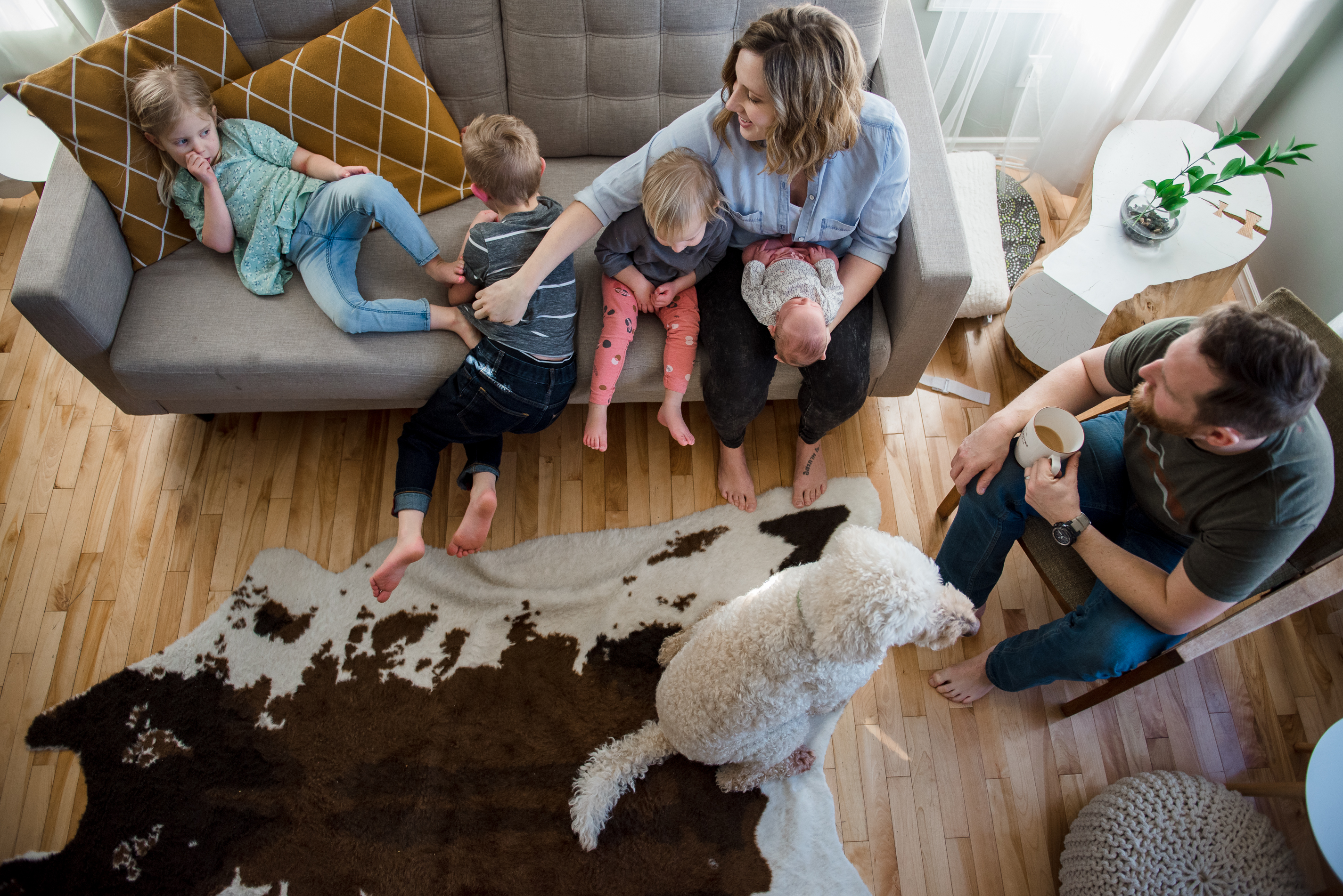 An overhead shot of a family in their living room with 3 older siblings and a new baby