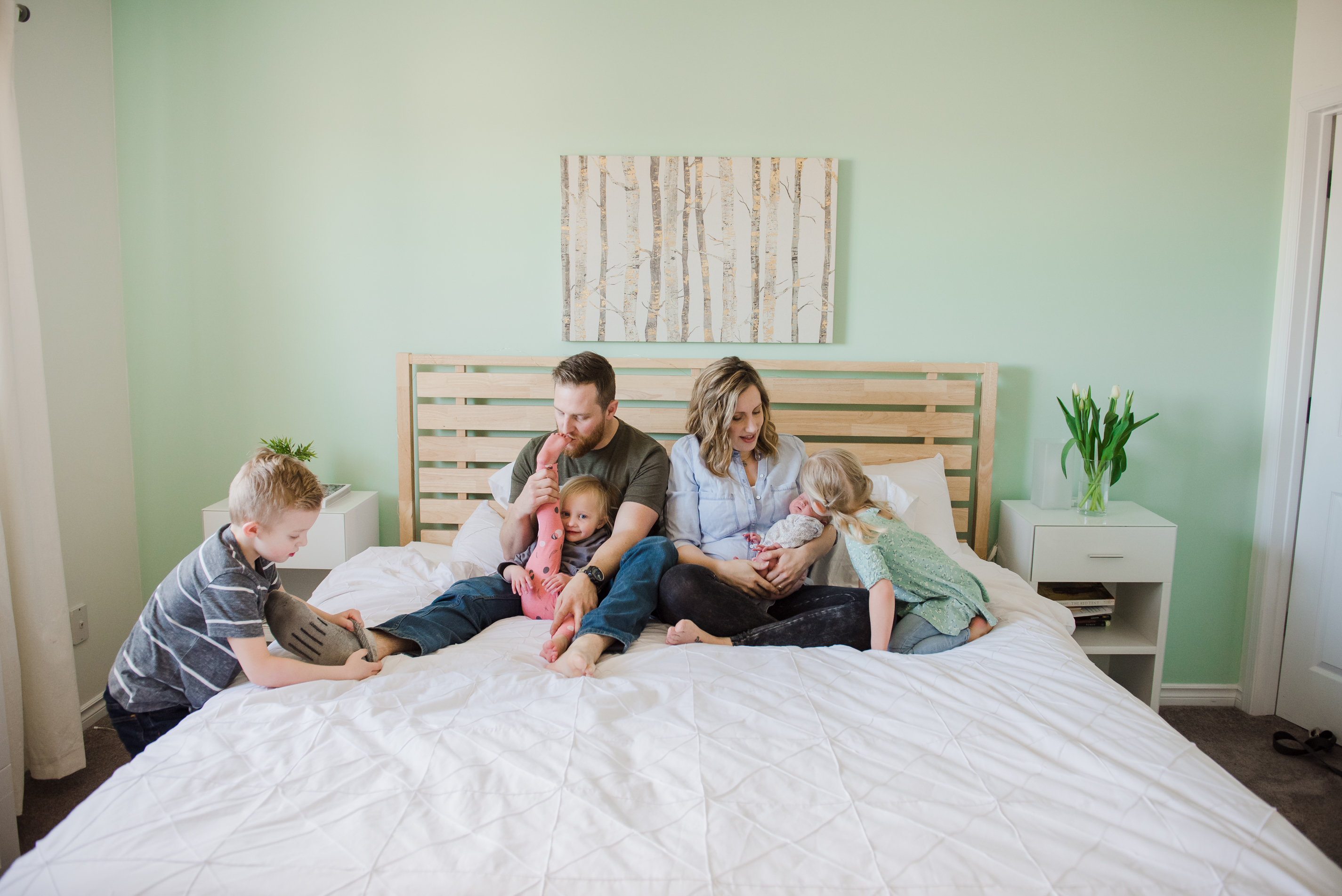 A family hangs out on a bed during their newborn photo session in Sherwood Park