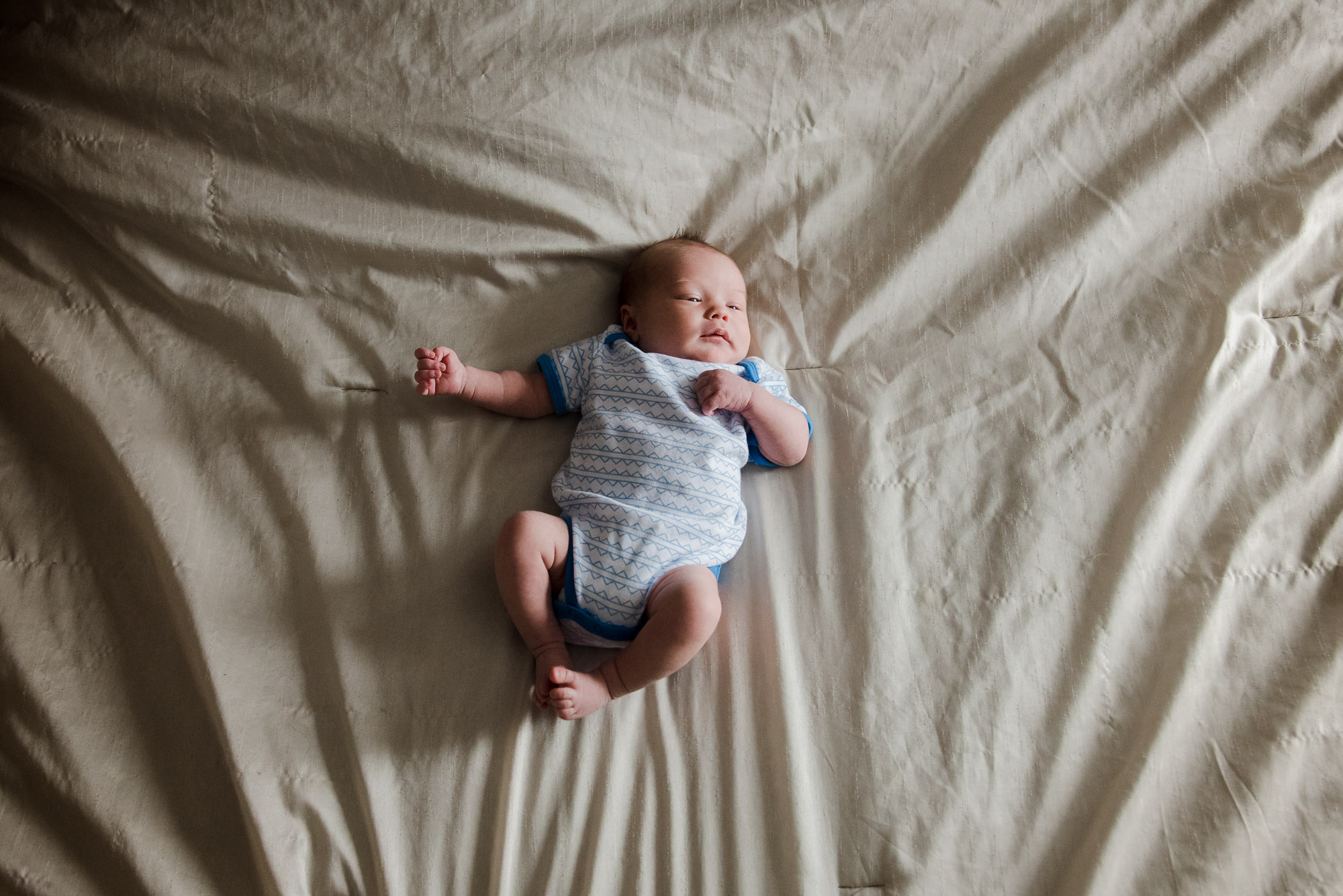 A newborn baby hangs out on a bed with crumpled sheets