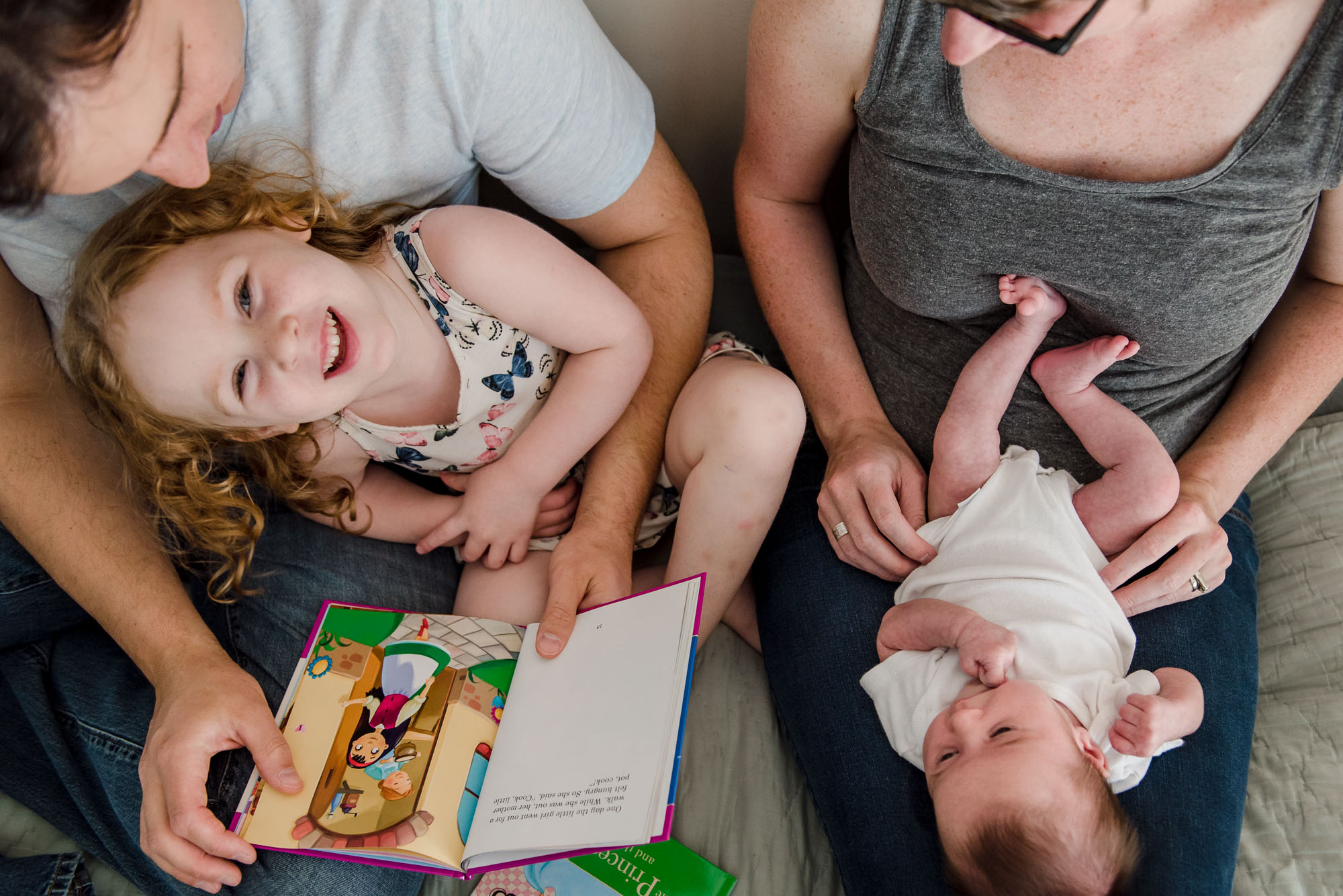 During a newborn photo session, a family hangs out on the bed and reads