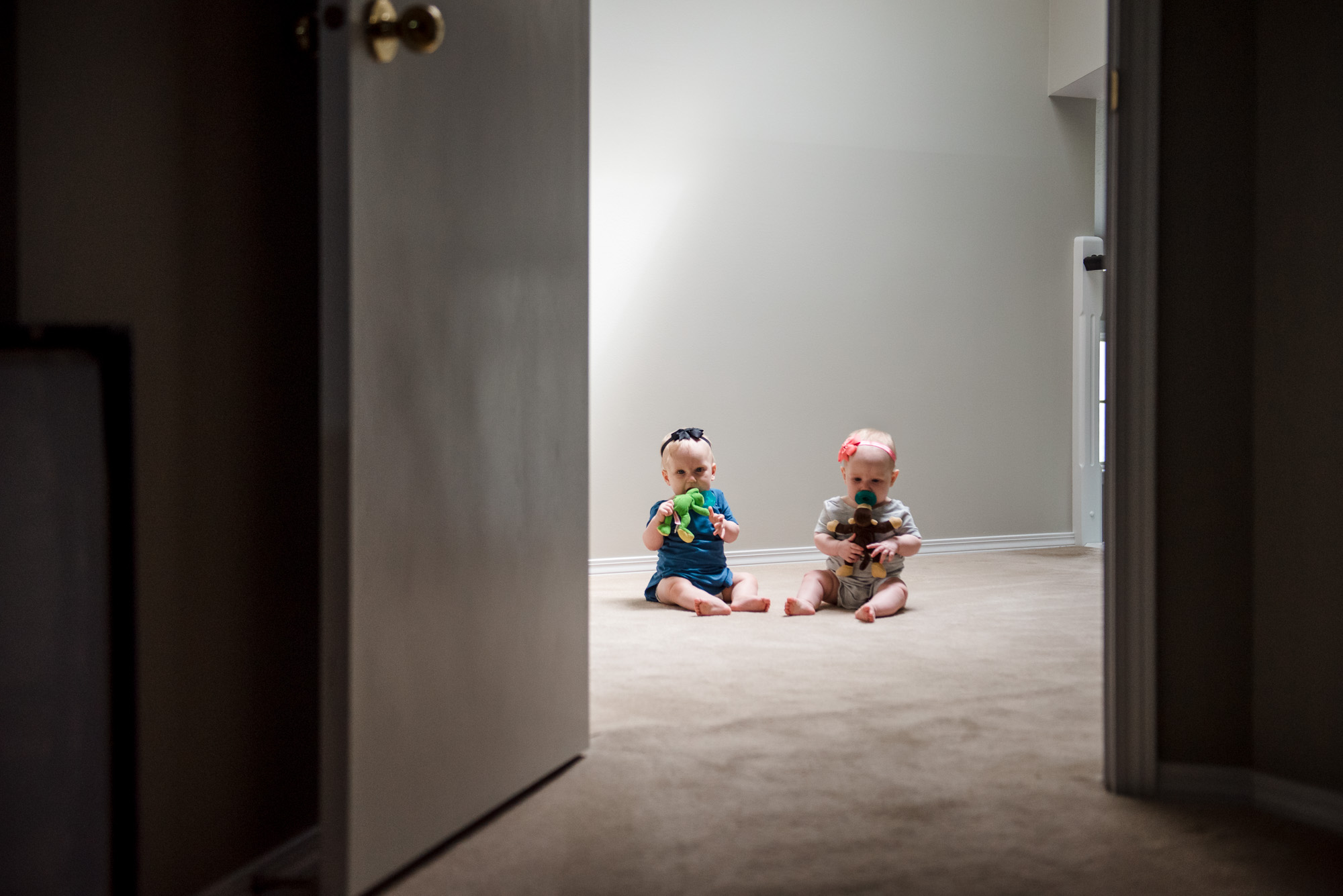 2 twin baby girls sit in the hallway of their new home. 