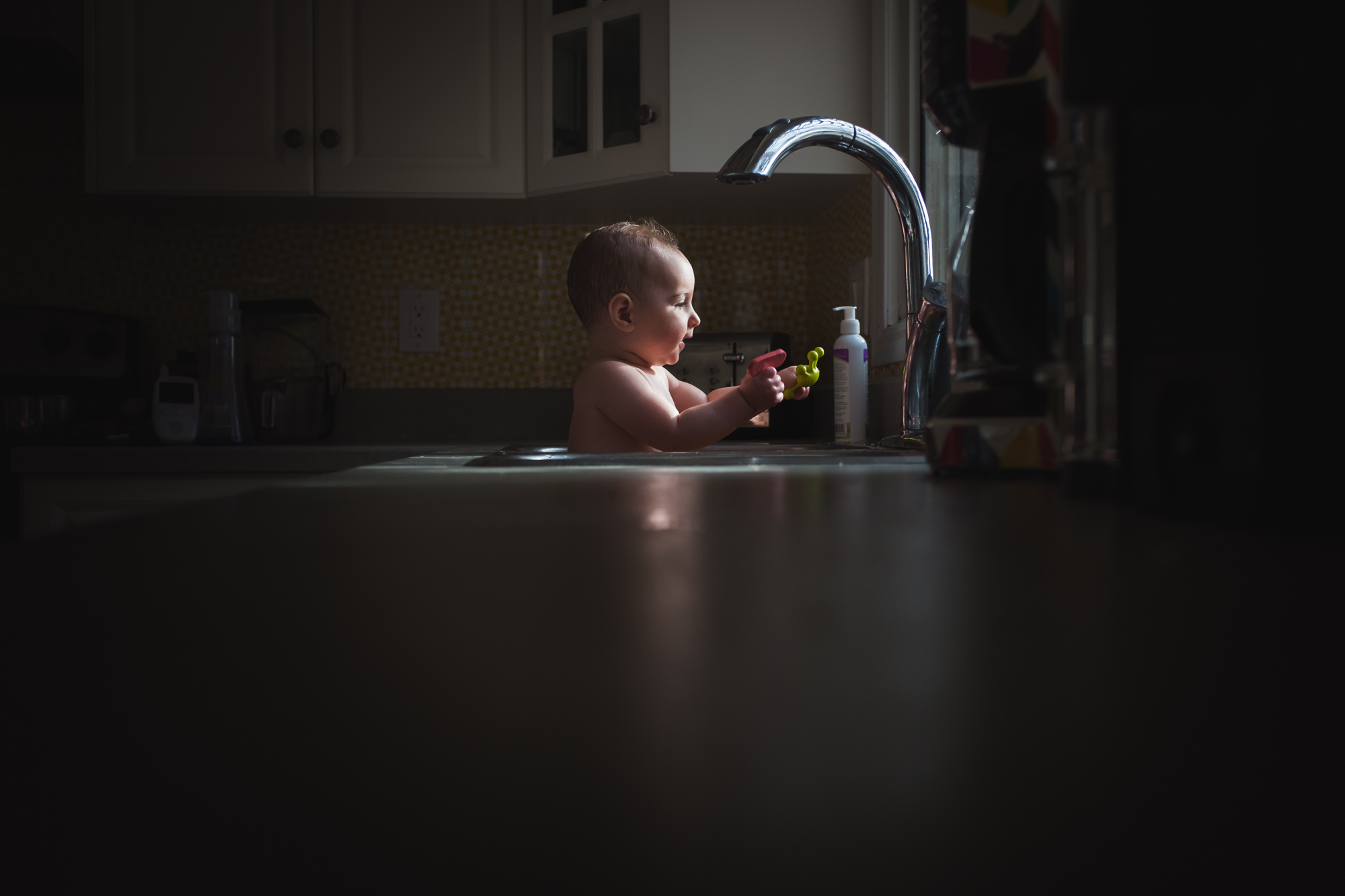A baby bathes in a kitchen sink