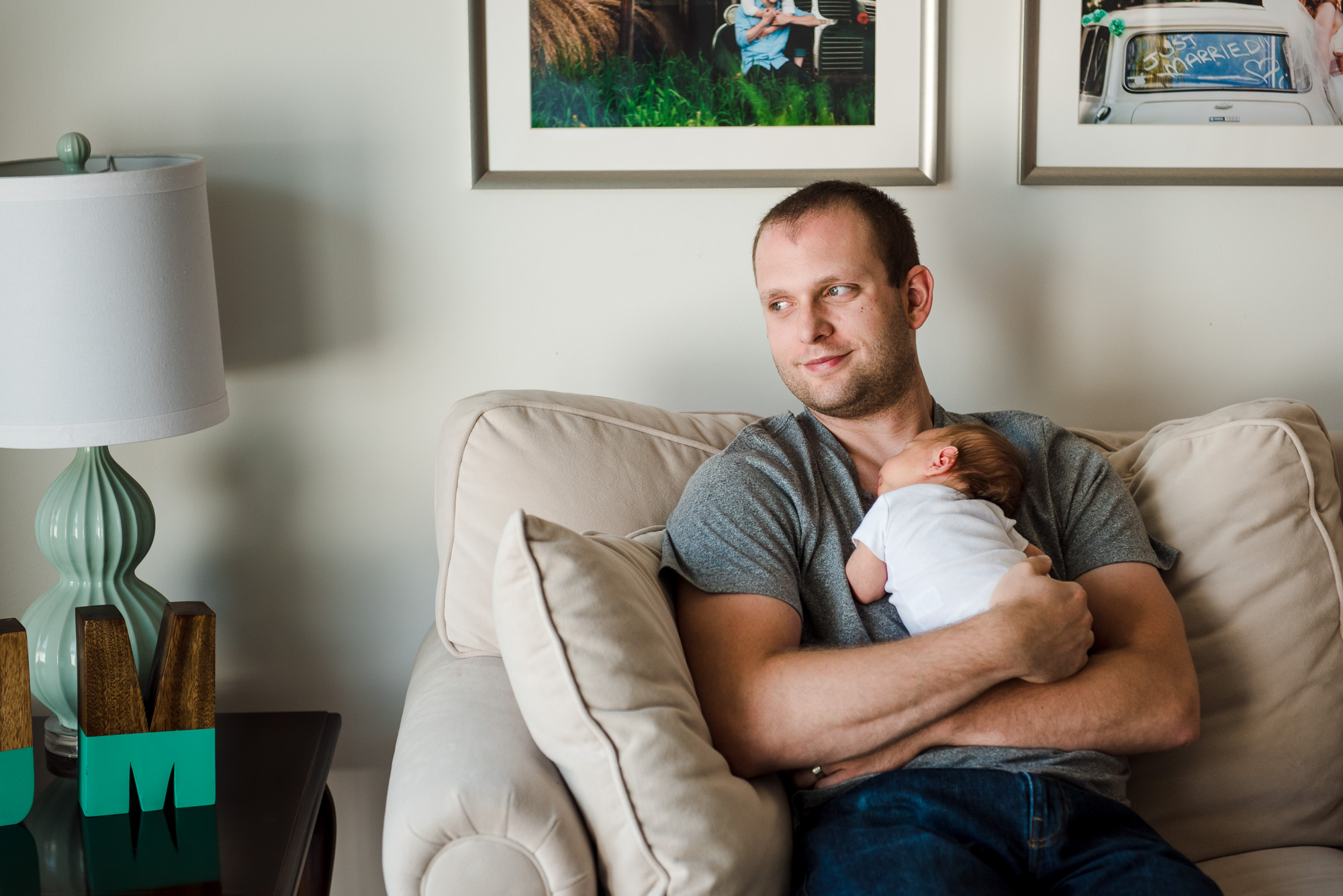 A dad sits and looks out a window with his newborn baby girl
