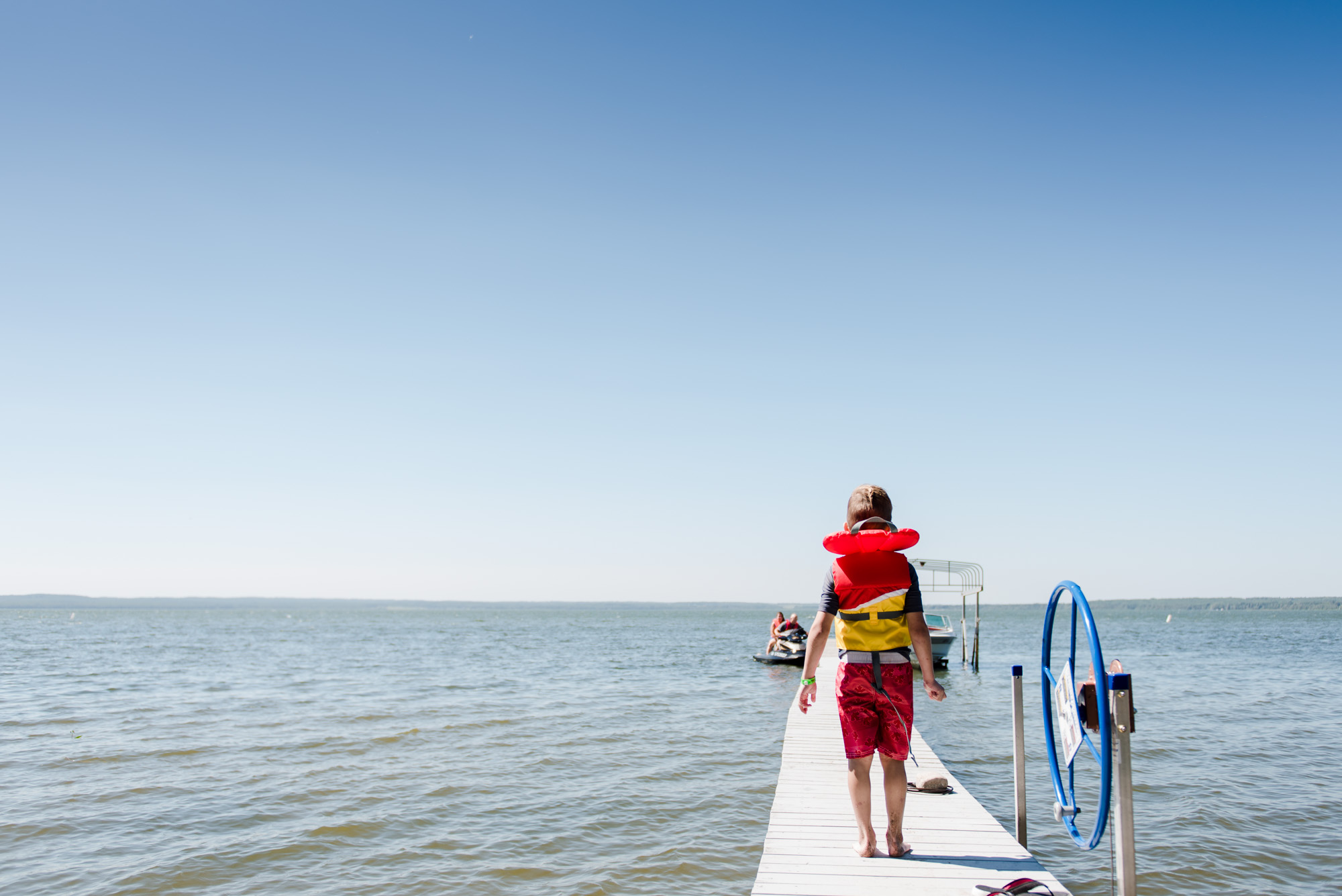 A boy stands on a dock at Pigeon Lake, Alberta during a fun family photo session