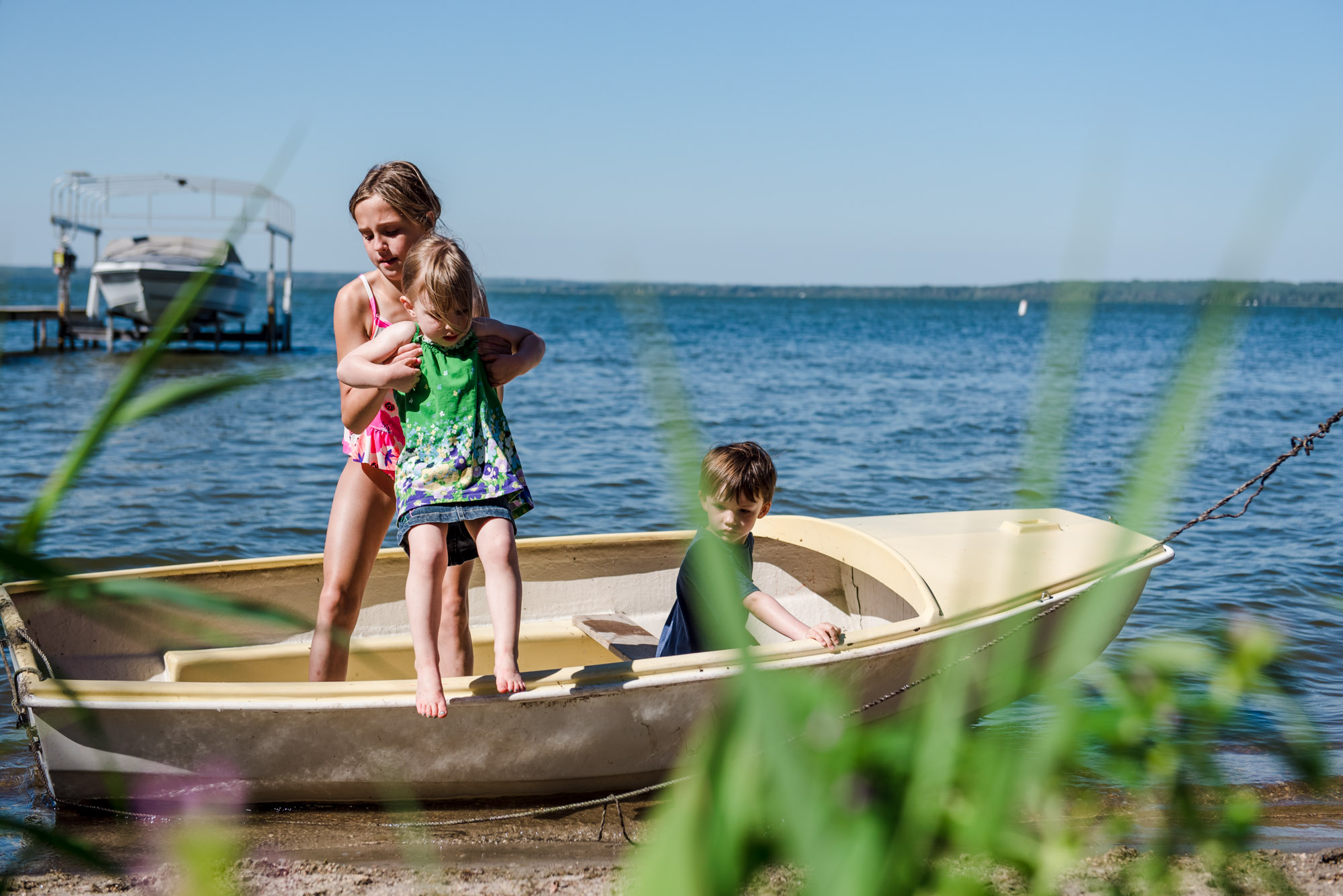 A young girl helps a little girl out of a boat on pigeon lake during a family photo session