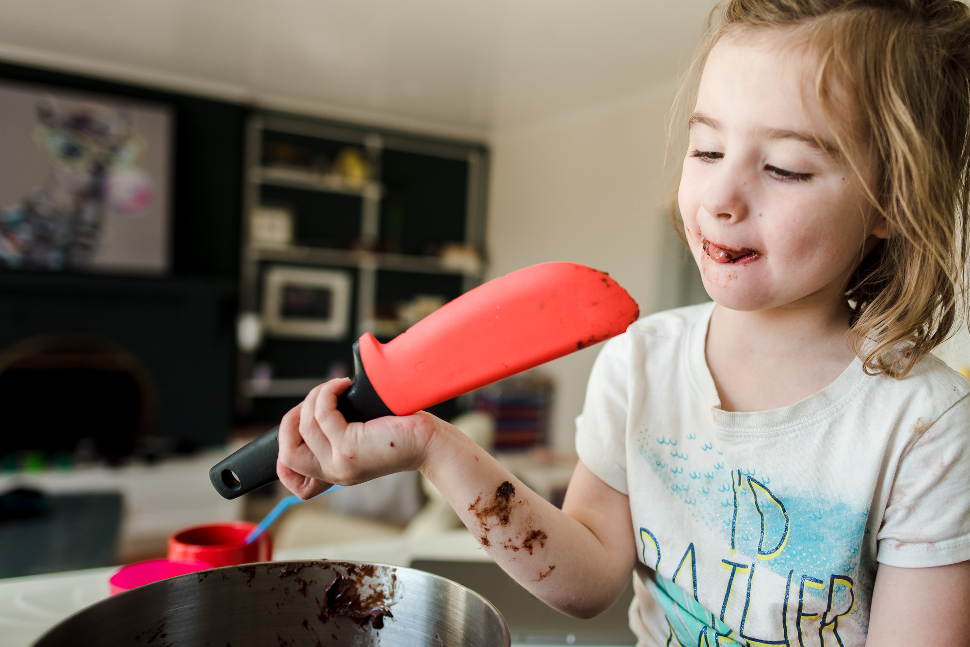 A little girl licks brownie batter. Edmonton photography mentoring