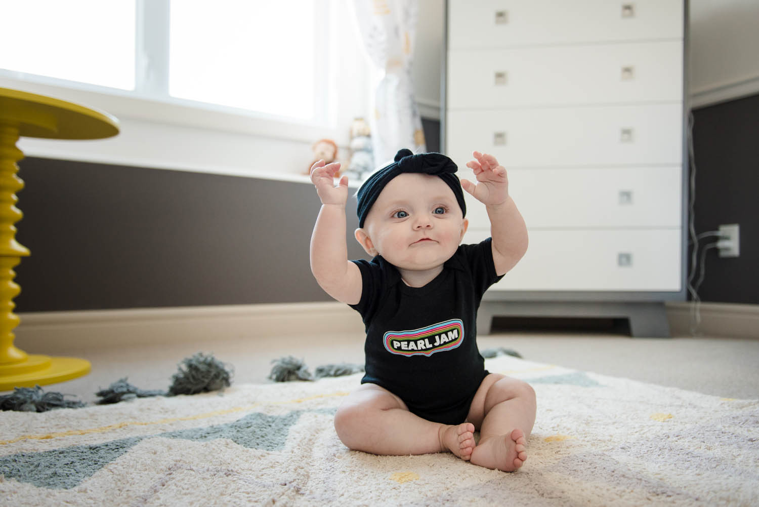 an adorable baby wearing a Pearl Jam shirt raises her hands during an 8 month photo shoot. 