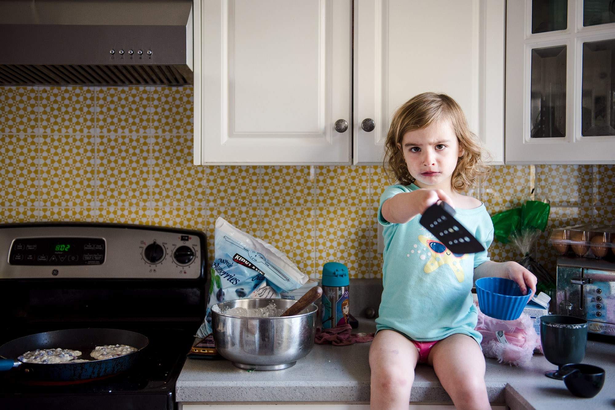 A little girl sits on a counter while easy protein packed pancakes made with cottage cheese cook on the stove.