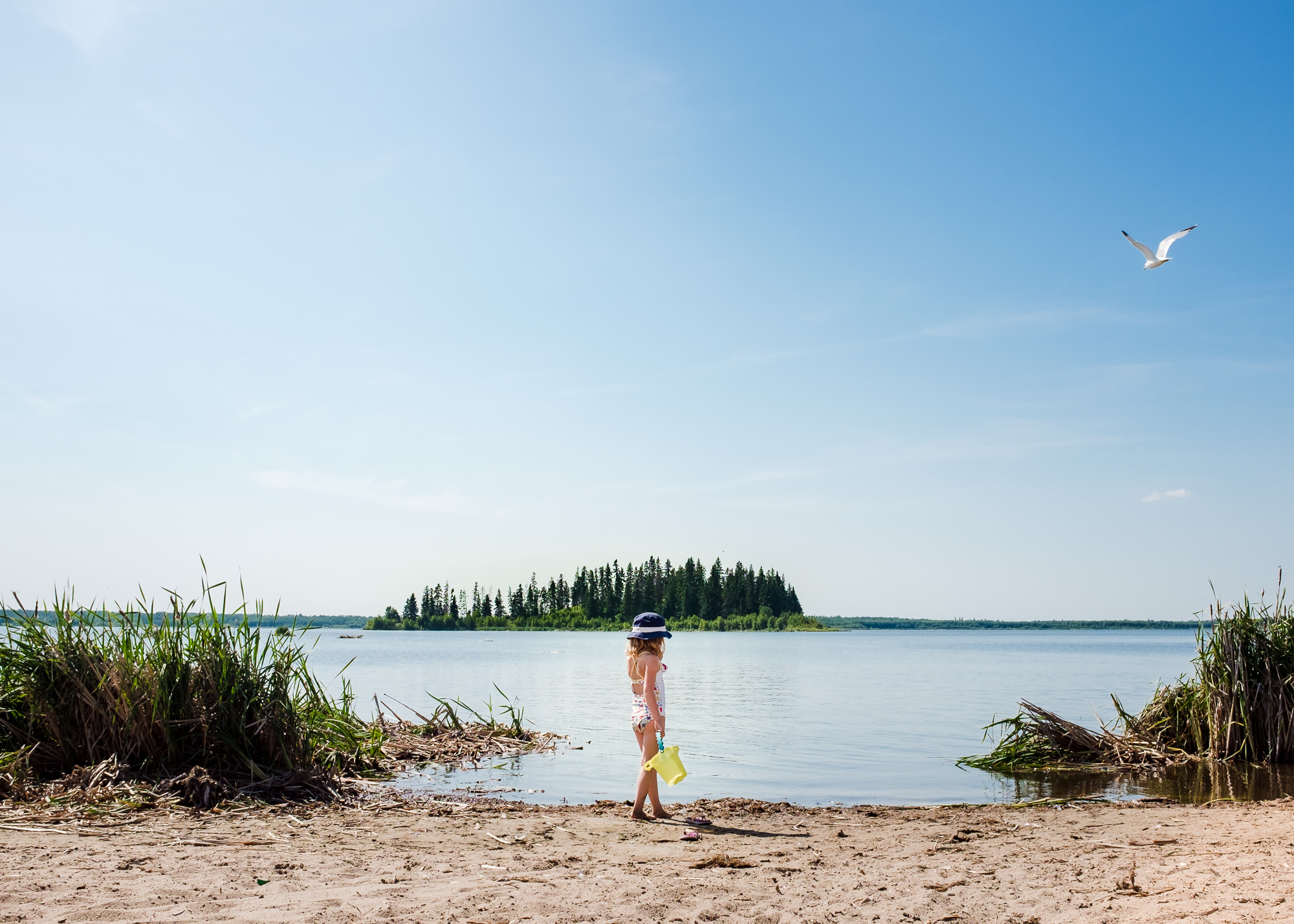 A young girl stands on the beach of Astotin Lake at Elk Island National Park. 