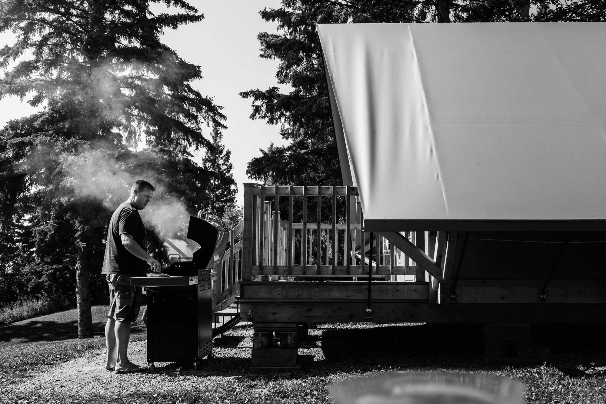 A father barbeques outside of a comfort camping Otentik at Elk Island National Park