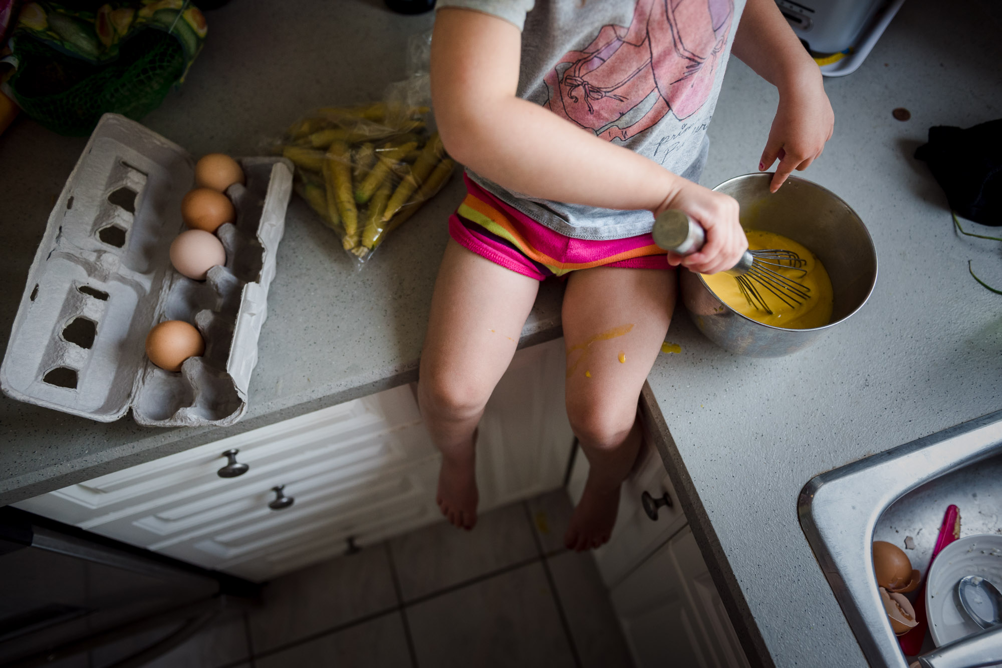 A little girl makes scrambled eggs while sitting on a countertop