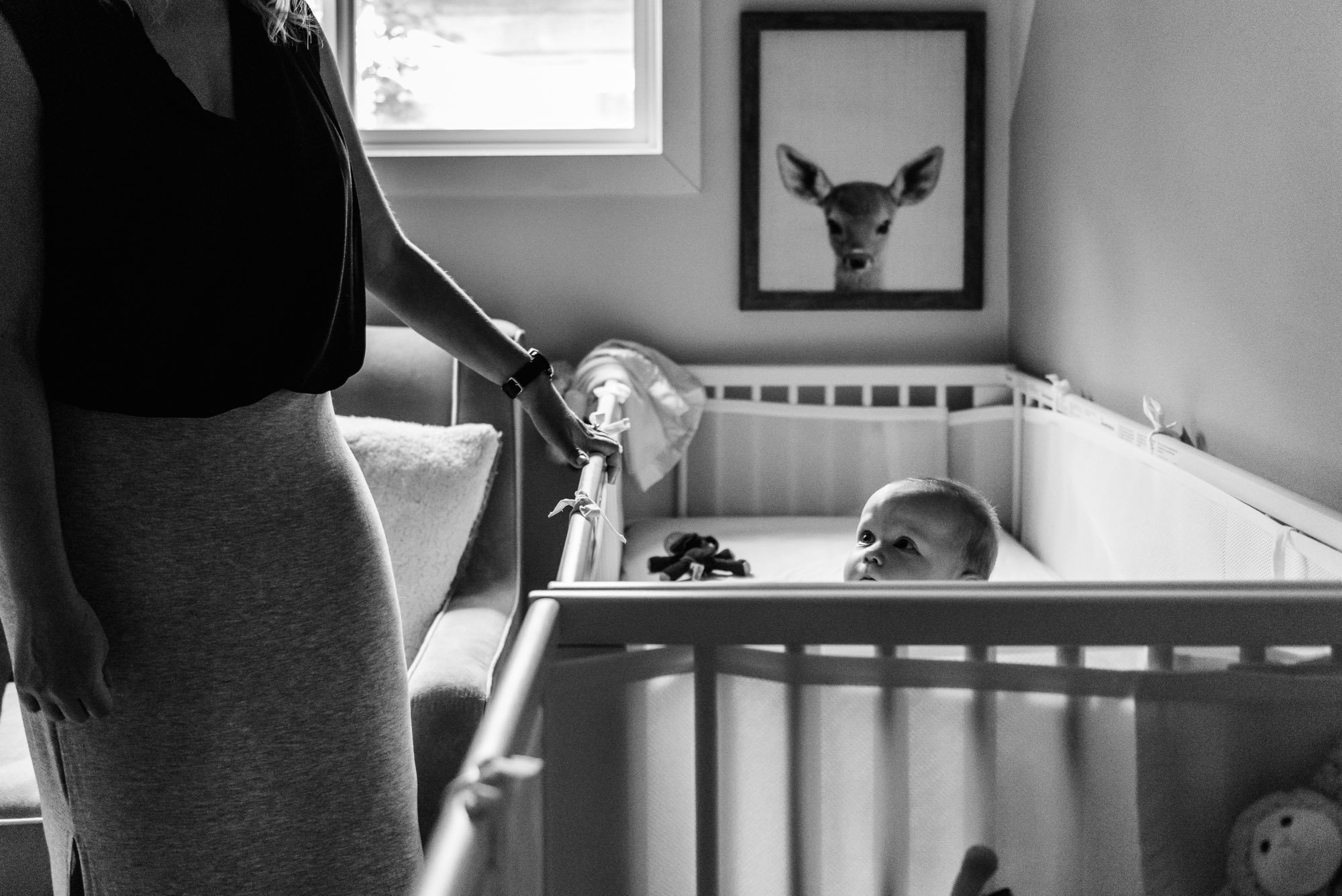 A mom stands beside her baby's crib during an Edmonton family photo session