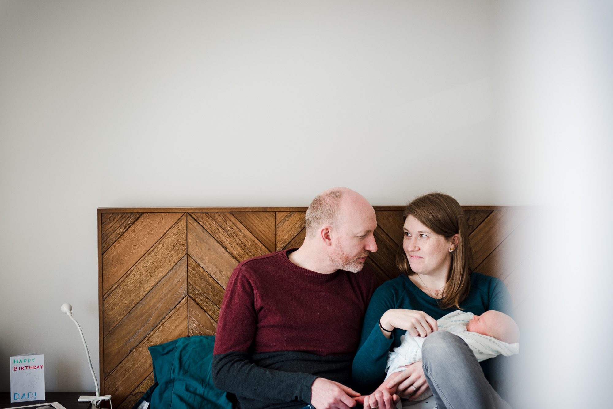 a couple sits on their bed with their new baby during a lifestyle newborn photo session in Edmonton