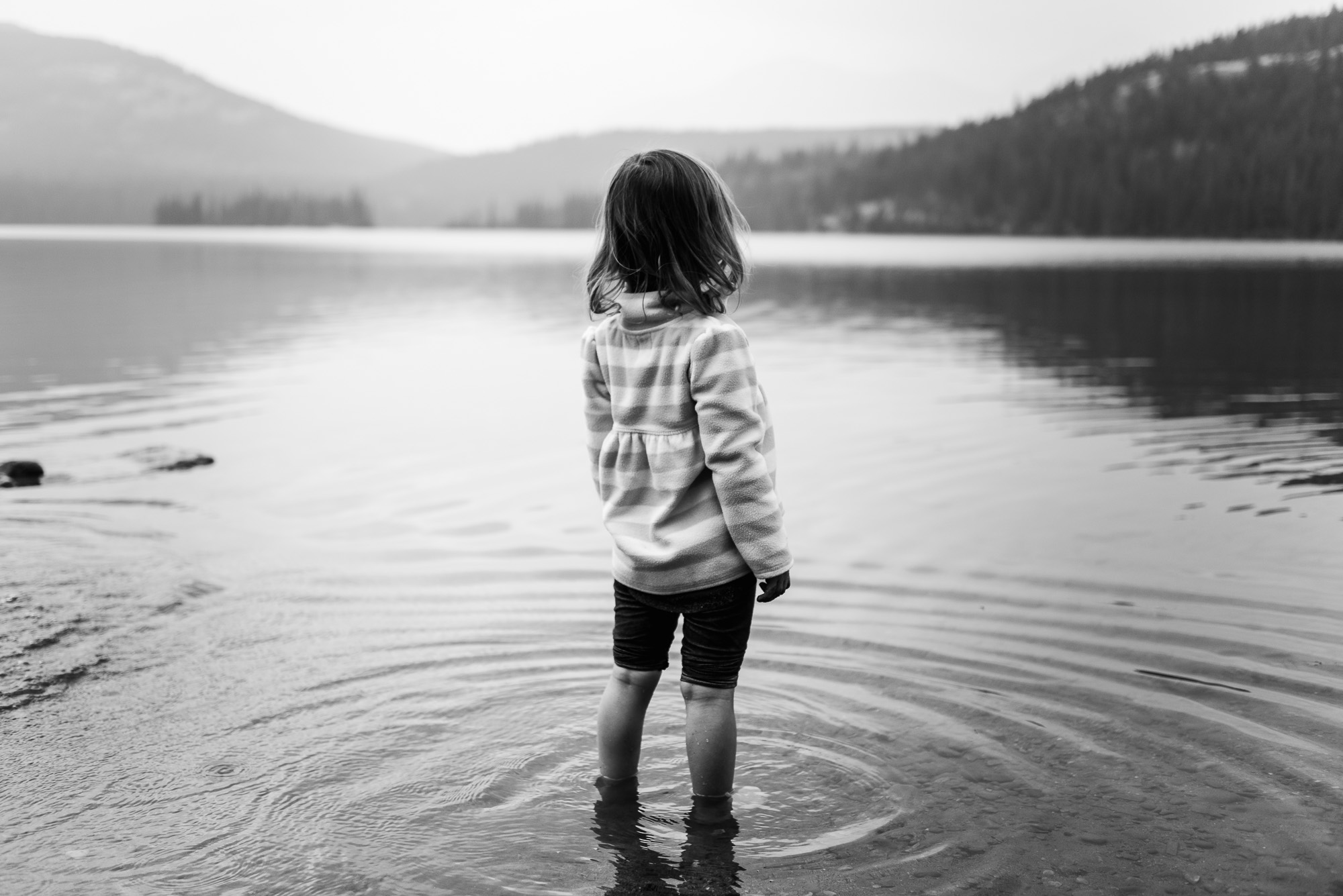 A girl stands in Pyramid Lake in Jasper National Park with ripples surrounding her legs. 