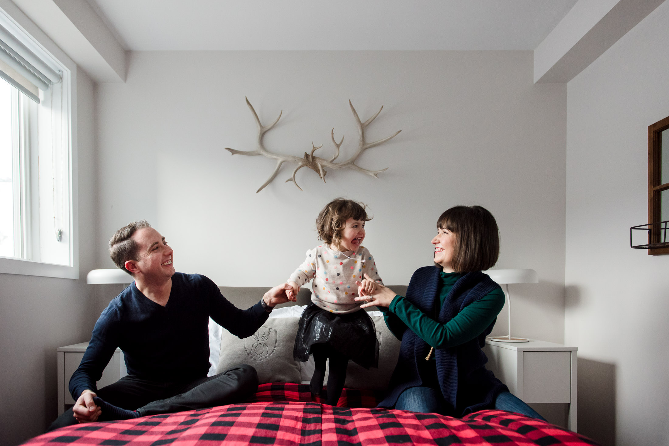 A girl jumps on the bed with her parents during christmas photo session