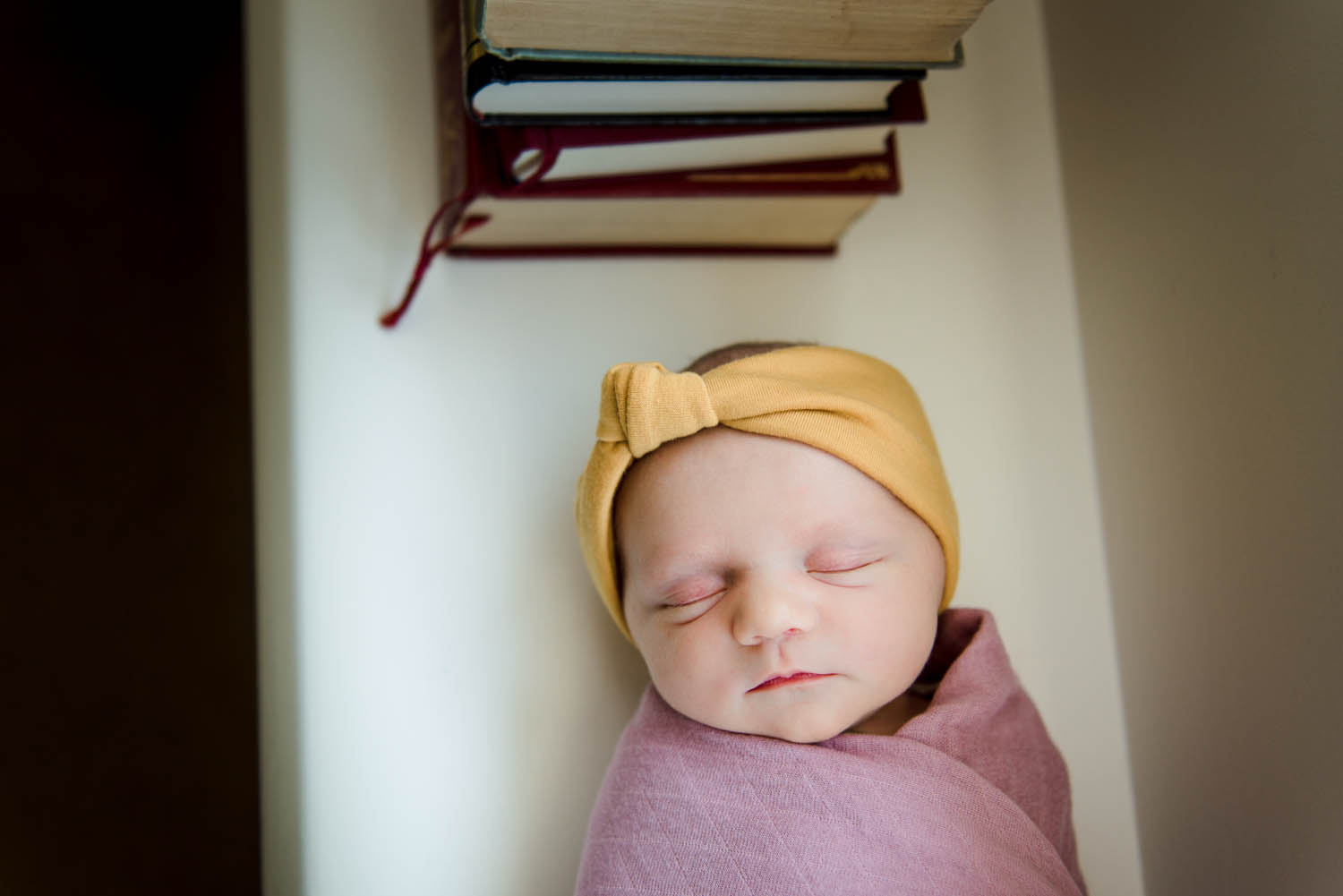 A newborn baby swaddled beside books during pictures in her sherwood park home