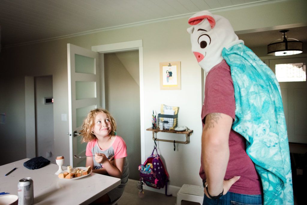 A dad wears a blanket on his head making his daughter laugh during breakfast