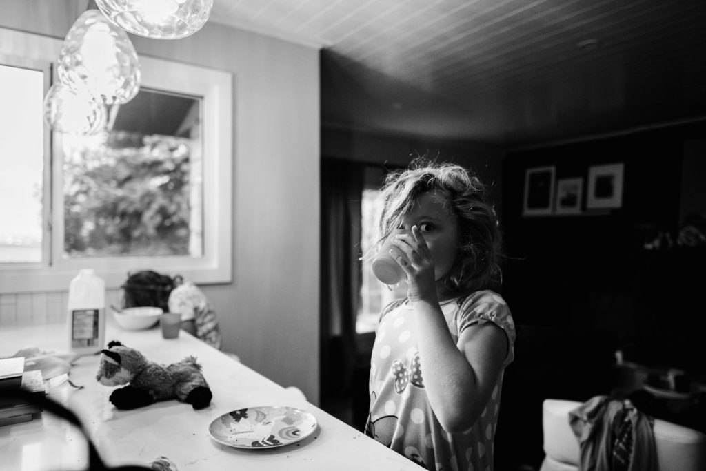 A girl drinks water while eating breakfast in her home as part of Fiddle Leaf Photography's before breakfast series