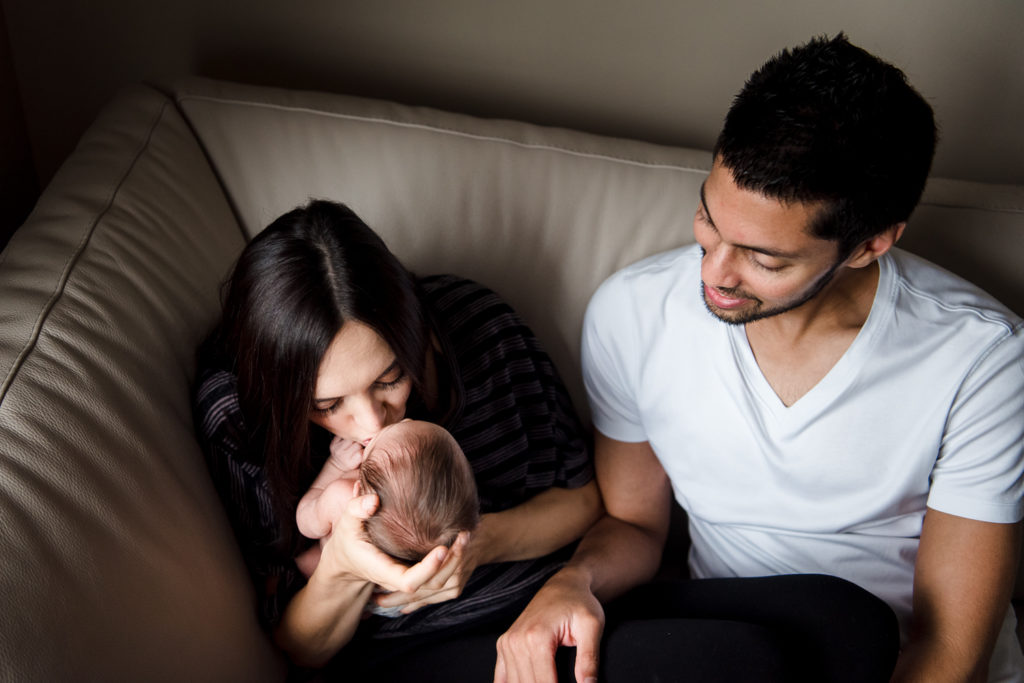 a mom kisses her newborn baby while dad watches on