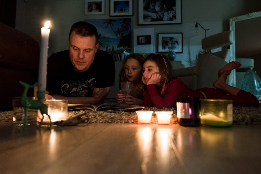 Girls read Christmas books with their dad by candle light