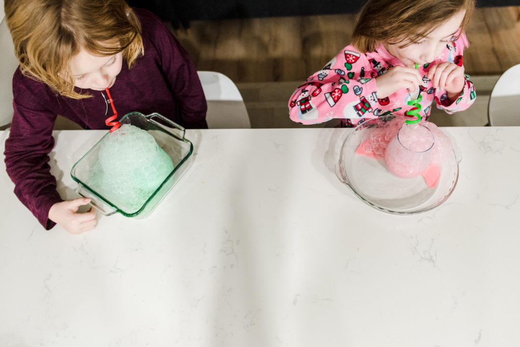 Girls blow bubbles in milk for a Christmas activity advent calendar. 