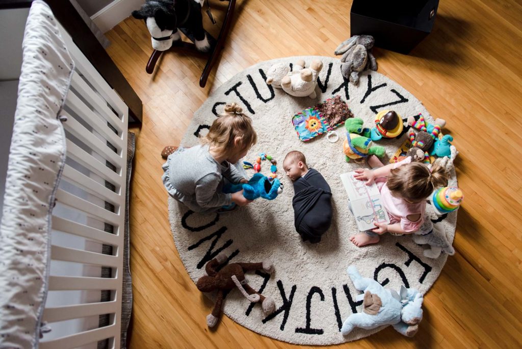 Sisters show their new brother their toys during an Edmonton lifestyle newborn photo session