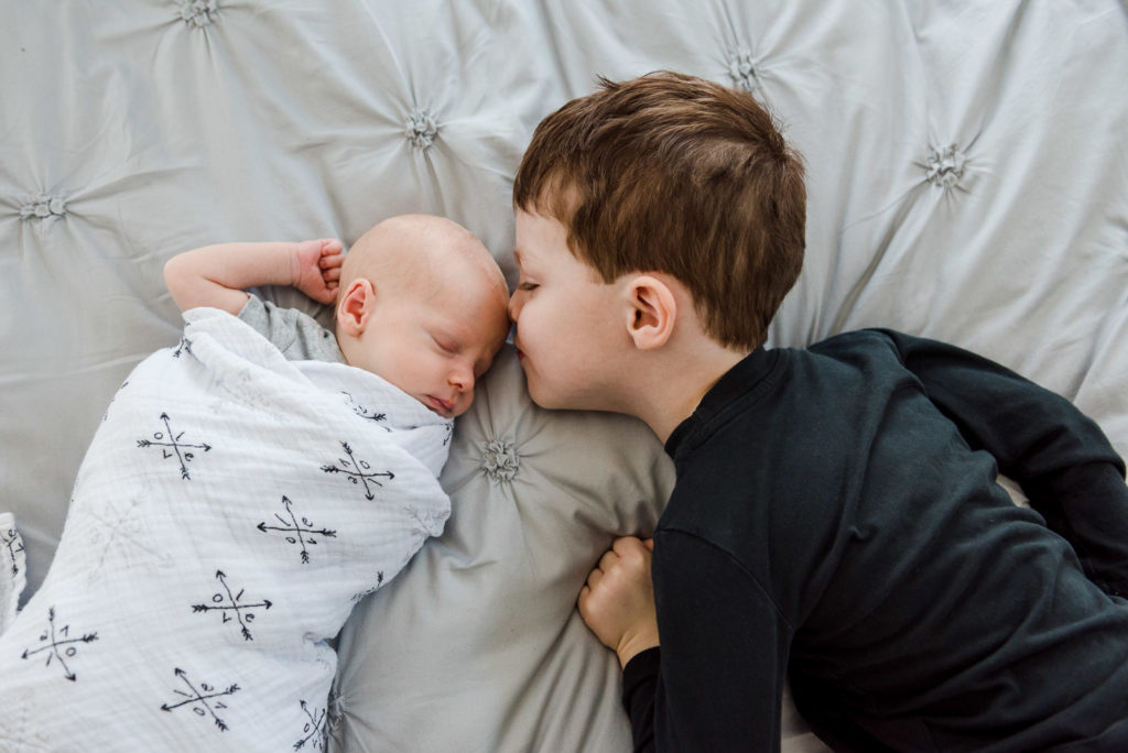 A newborn photo session with a sibling where the big brother snuggles into the new baby

