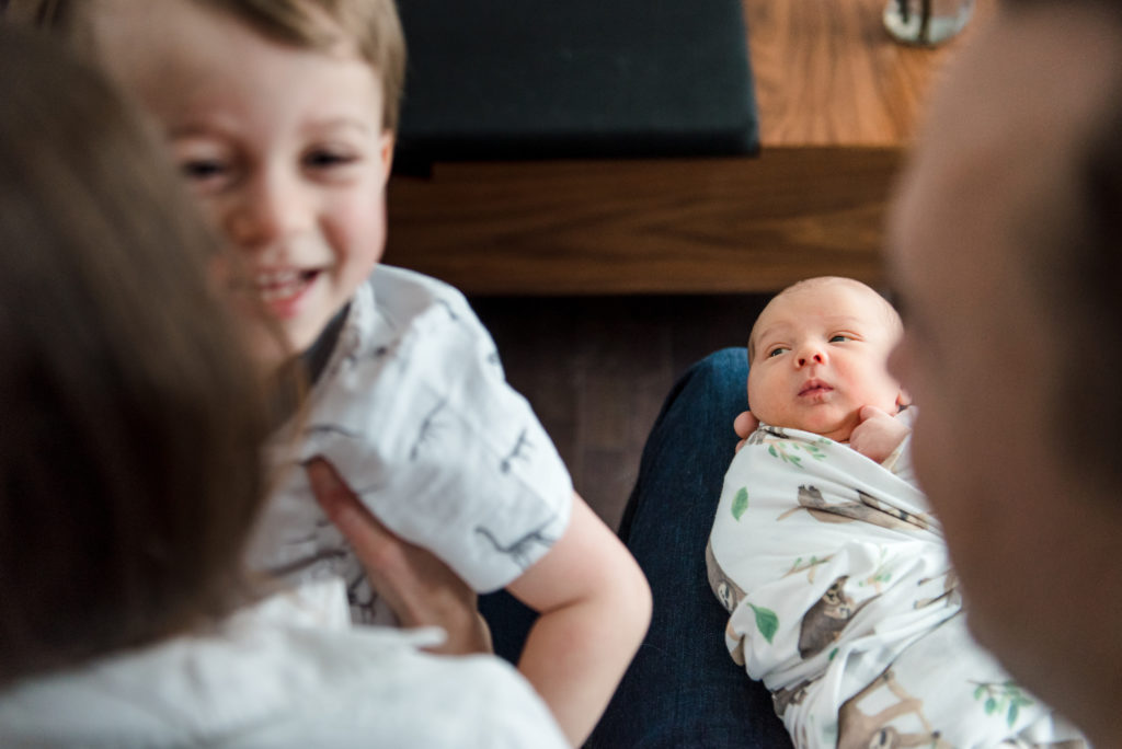 A big brother plays near by his newborn baby brother during a lifestyle newborn session by Edmonton photographer Fiddle Leaf Photography 