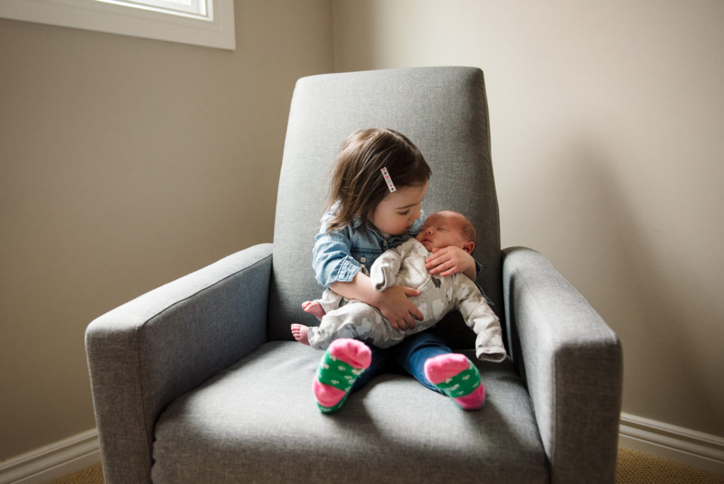 A little girl holds her newborn baby sister during her St. Albert newborn photo session