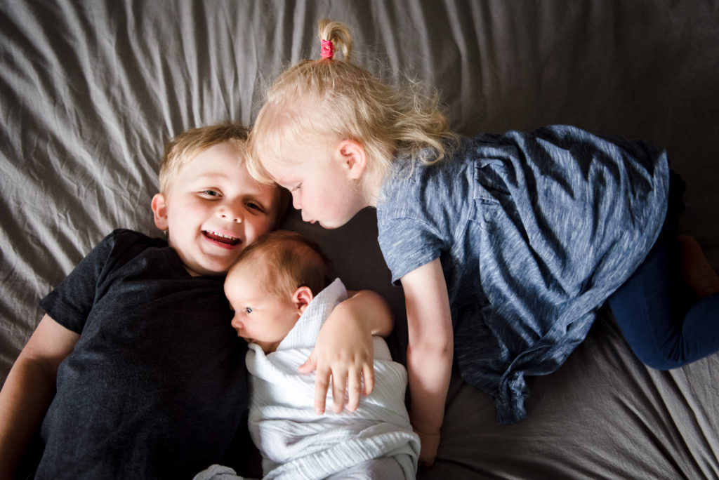 A set of siblings kiss a newborn baby during their Sherwood Park newborn photo session