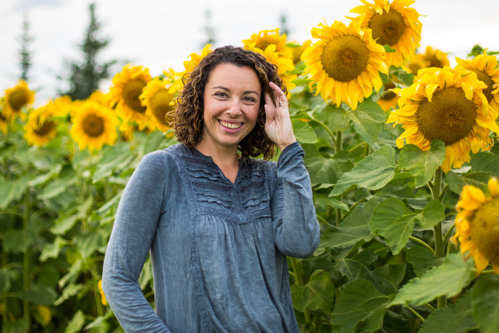 Edmonton family and newborn photographer Kelly Marleau of Fiddle Leaf Photography stands in an Edmonton sunflower field.