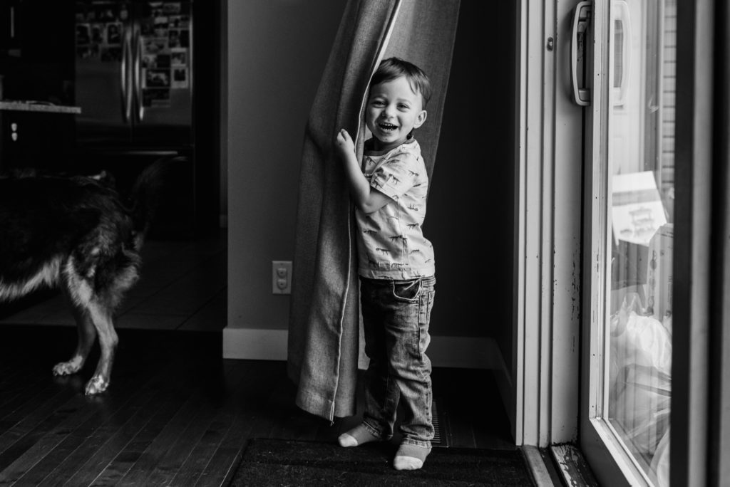 A little boy plays in the curtain during a documentary photo session in Edmonton by Fiddle Leaf Photography 