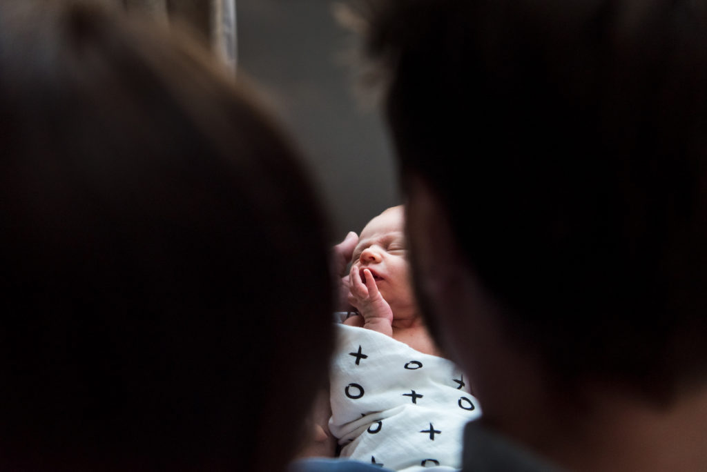 A newborn is framed by his parents in photo from one of the  top 100 female photographers to watch, Kelly Marleau of Fiddle Leaf Photography in Edmonton.