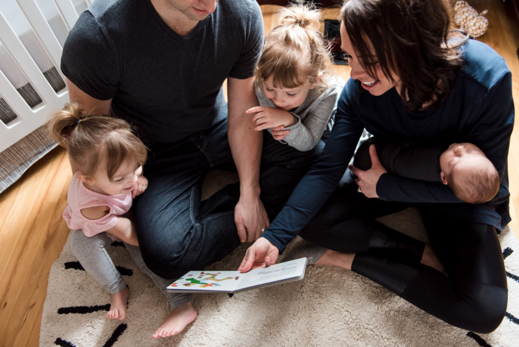A family gathers to read a book during a newborn photo session featuring a beautiful navy blue sweatshirt from Edmonton maternity Store, Yo Mama Maternity
