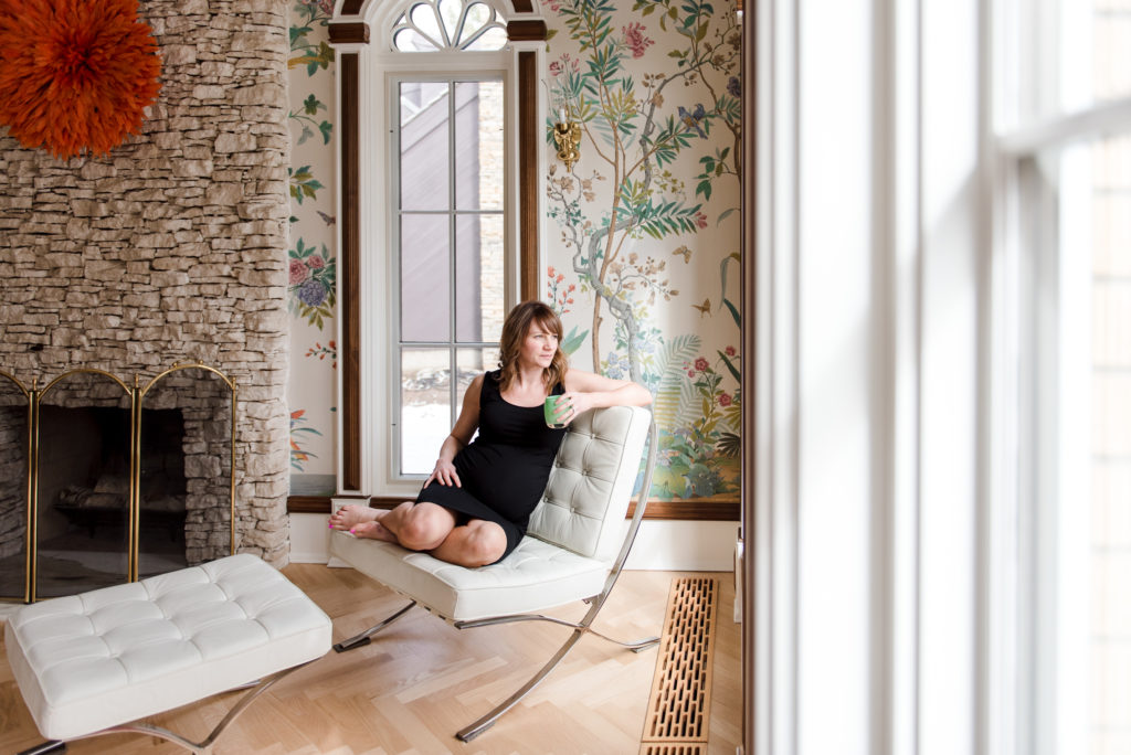 A mom sits in a flowered living room wearing a basic black maternity dress.
