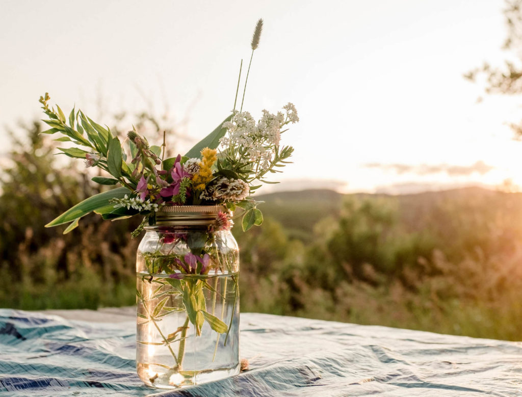 A mason jar of flowers sits on a picnic table
