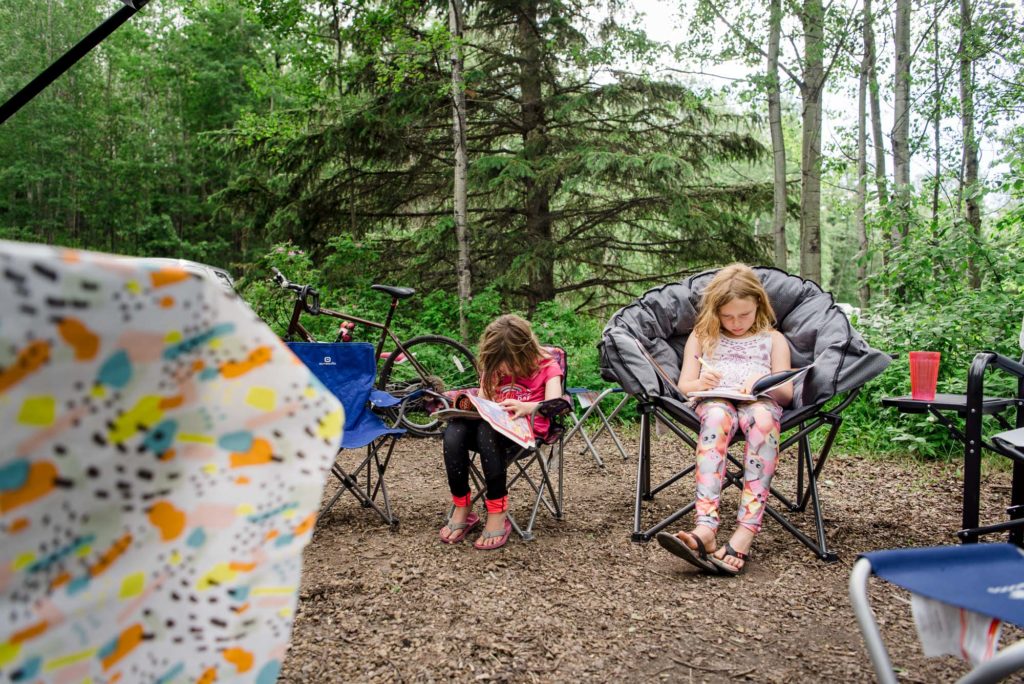 Sisters sit in a campsite doing sticker books. Things to bring camping with kids. 