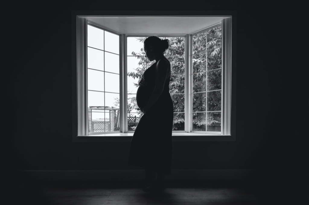 A black and white silhouette photograph of a pregnant woman in front of a window.