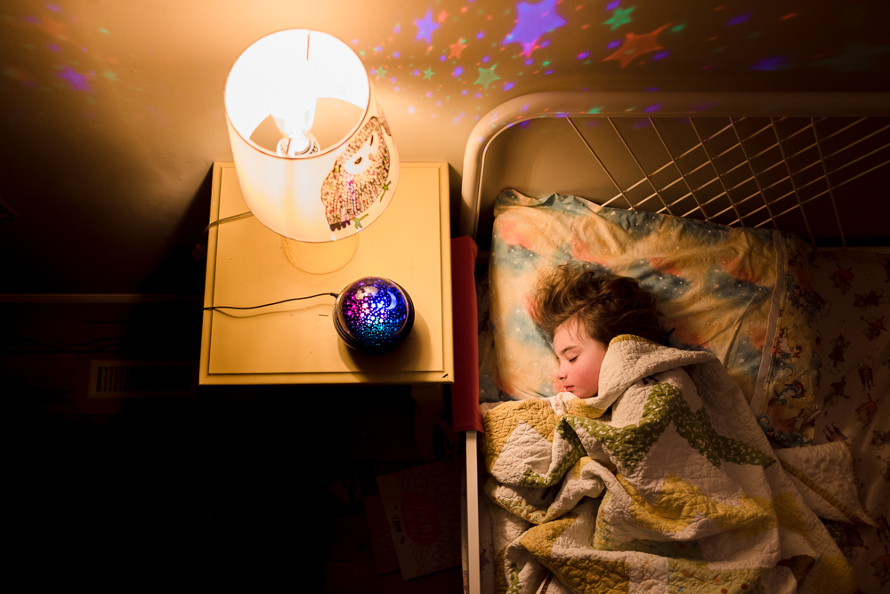 A little girl sleeps in her bed with a bedside lamp on, taken using a photo tip from Edmonton child photographer Kelly Marleau. 