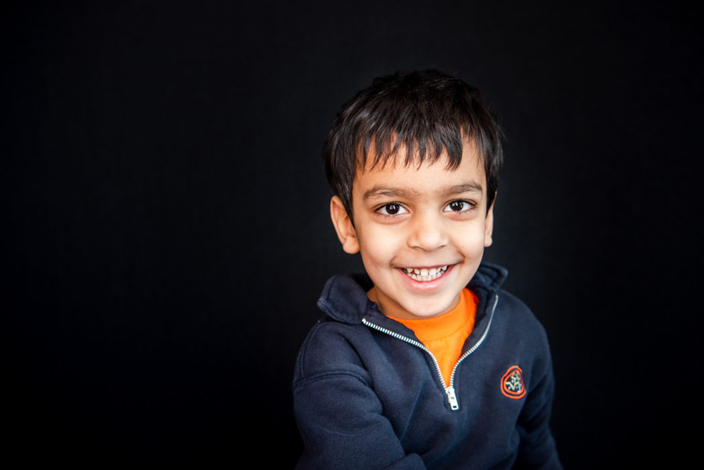 A little sits against a black background and smiles at the camera in a Kepler Academy sweater. 