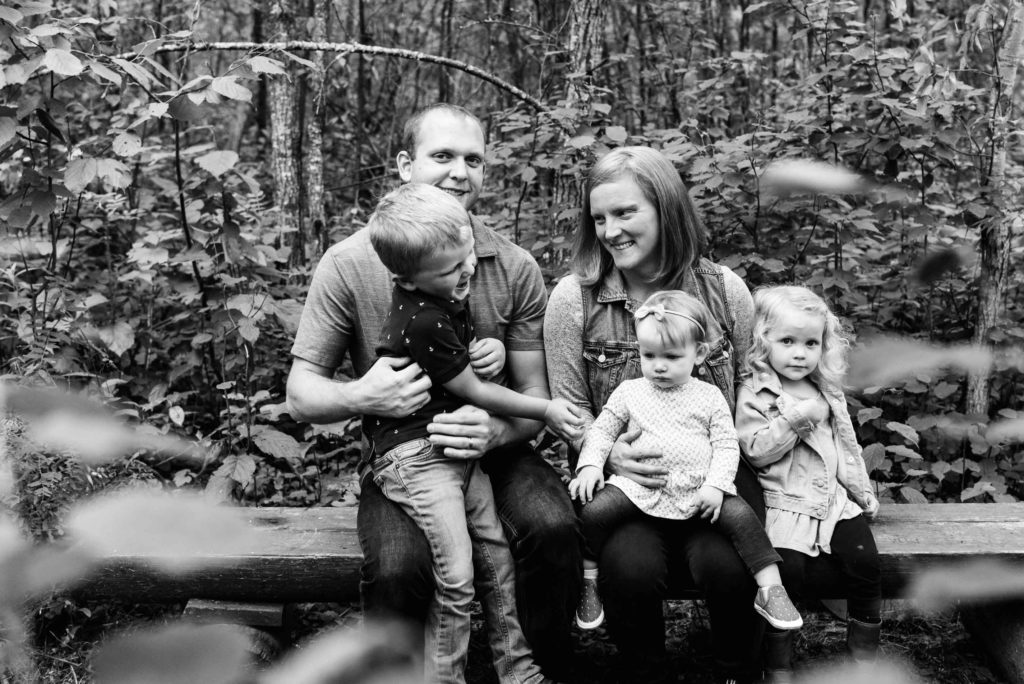 A family sits on a bench laughing together during a family photo session in Sherwood Park, Alberta. Sherwood Park Natural Area