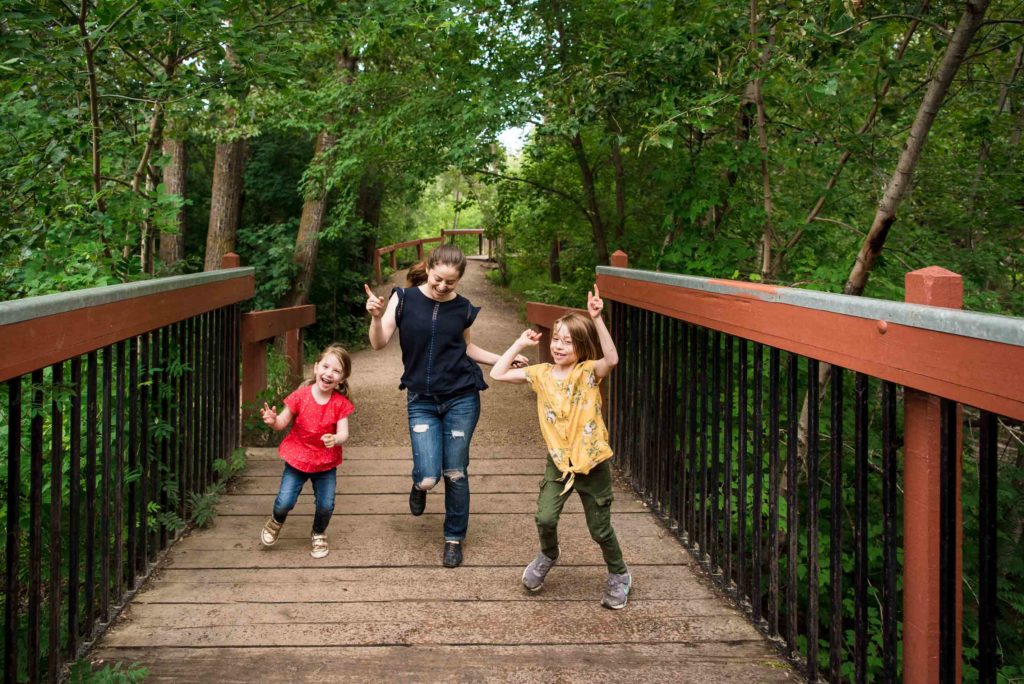 Family photos in Mill Creek Ravine. A mom and her daughters dance during a family photo session in Edmonton's Mill Creek Ravine. 