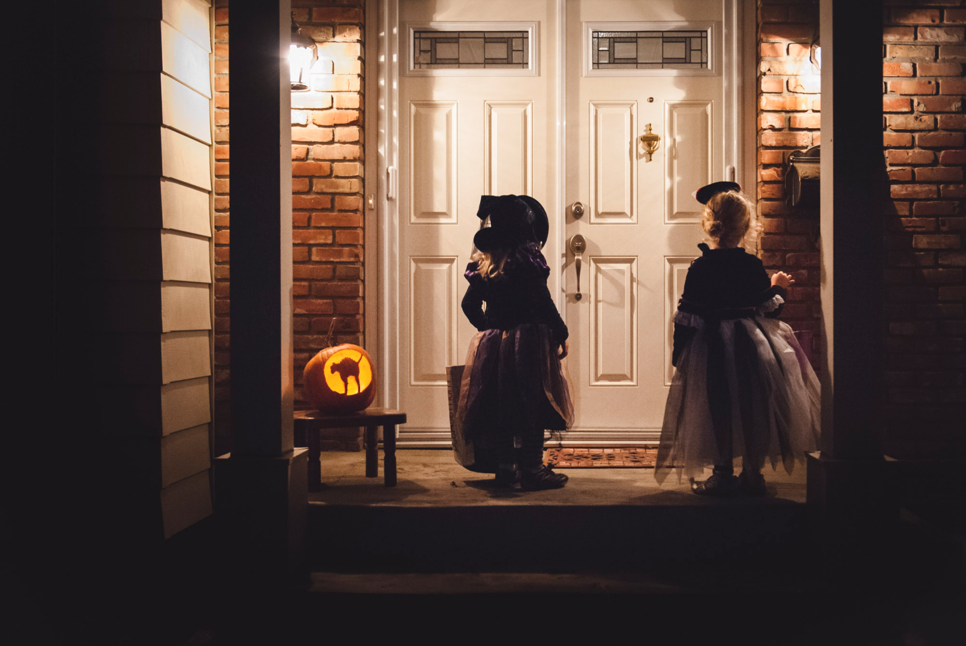2 girls stand at a door trick or treating during Halloween in Edmonton. Halloween photo tips
