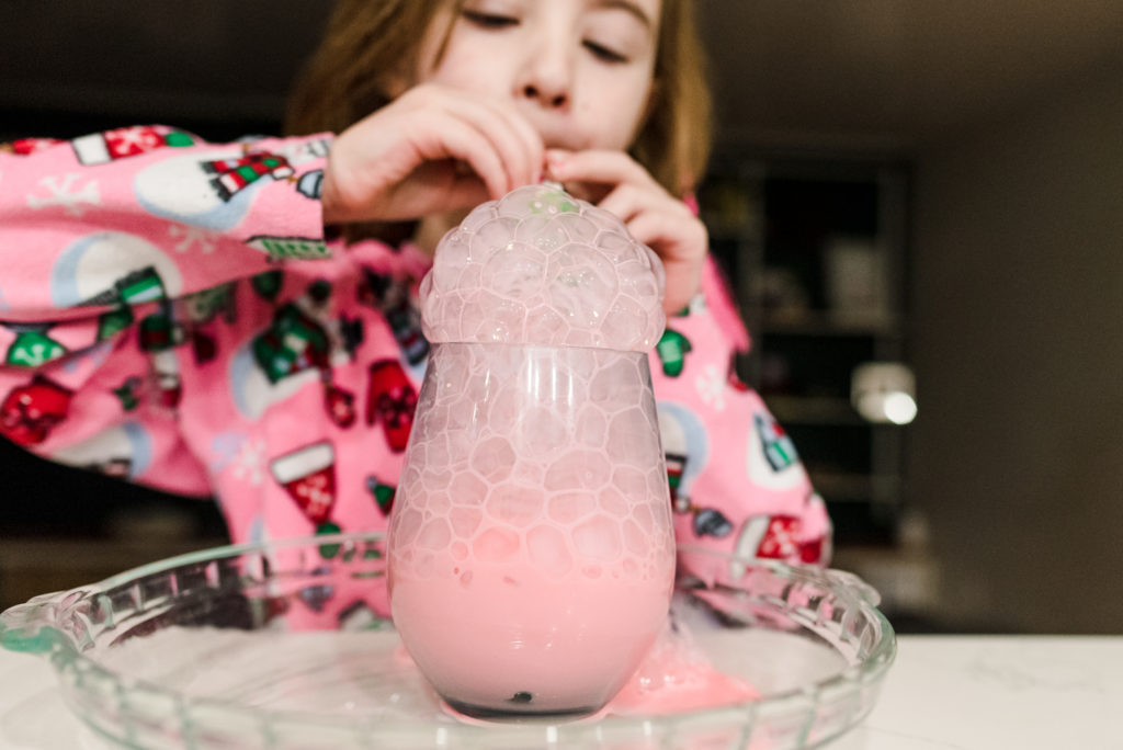 a girl blows milk bubbles as part of a christmas activity advent calendar. 
