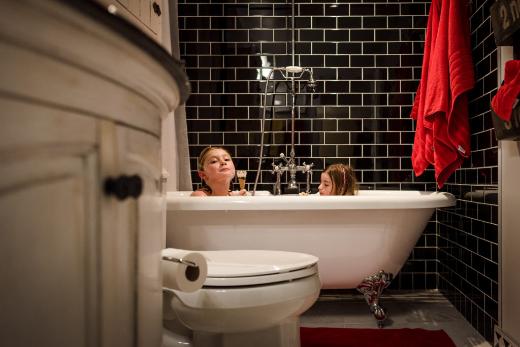 Sisters eat ice cream in the bath. 