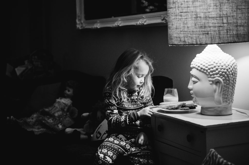 A little girl sits next to Santa's cookies and milk on Christmas eve. 