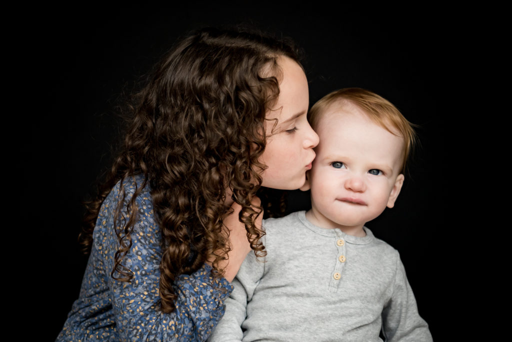 What to wear for school photos. Siblings in grey and light blue. a sister kisses her brother. 